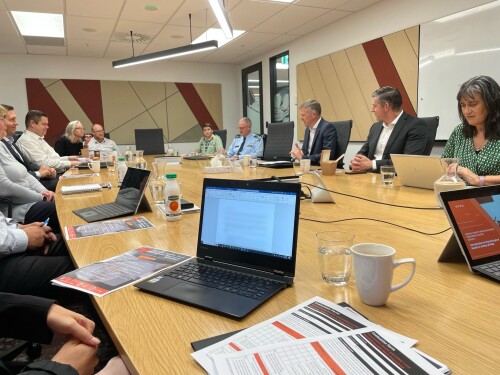 Meeting room table with people sitting around with their laptops and papers